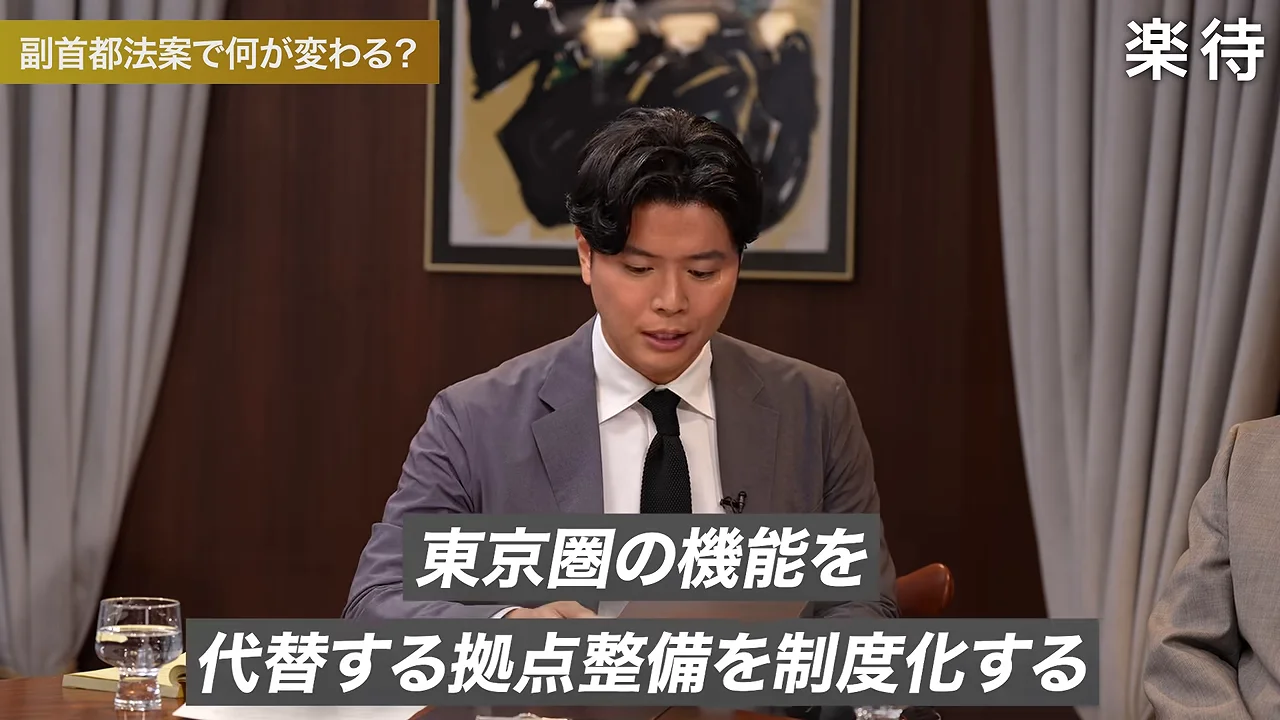 スーツを着た男性が机の上の資料に視線を向けながら話しています。