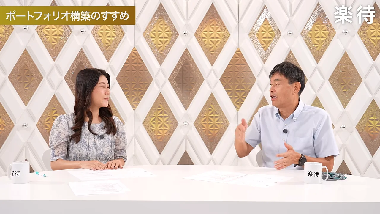 スタジオのテーブルを挟んで女性と男性が座り、男性が身振りを交えながら話している。